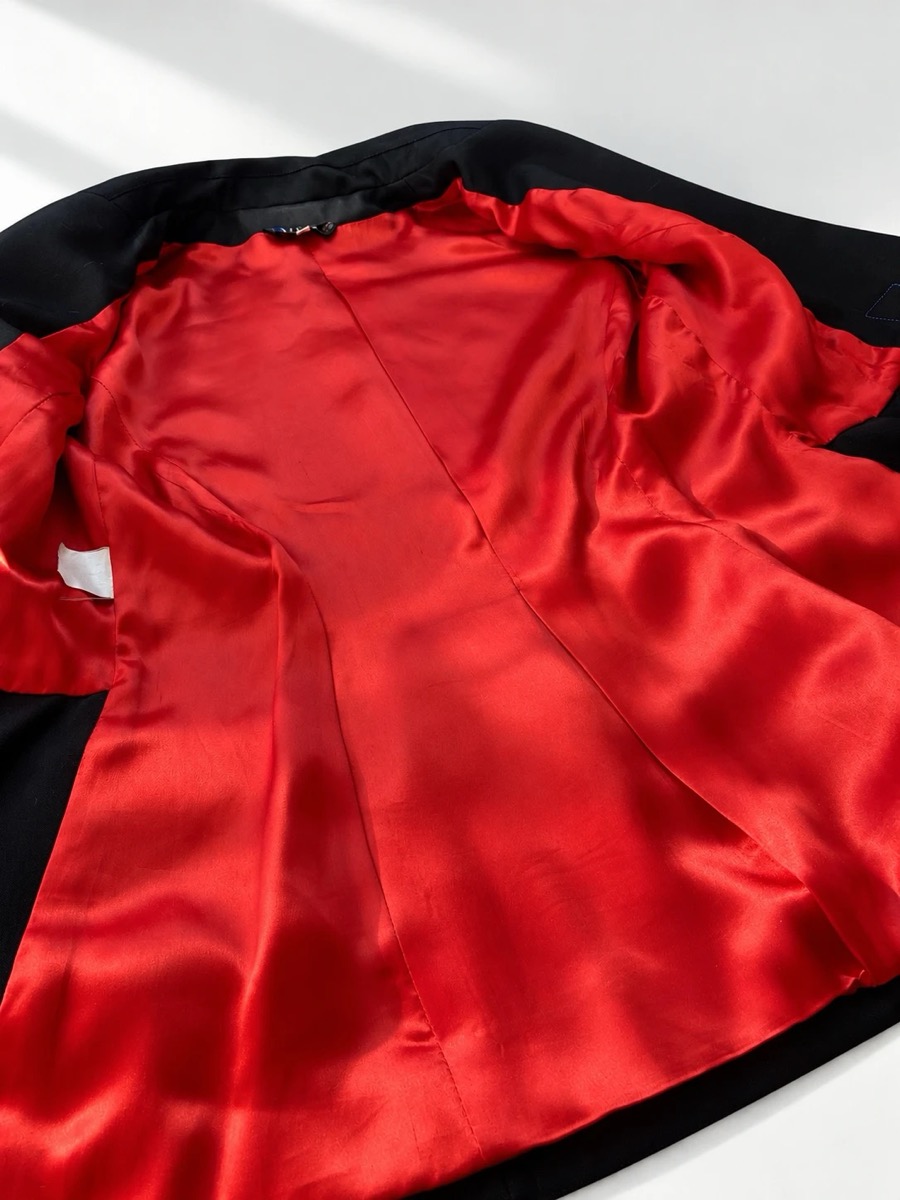 A black jacket laid open on a white table, showing its red satin lining and seams.